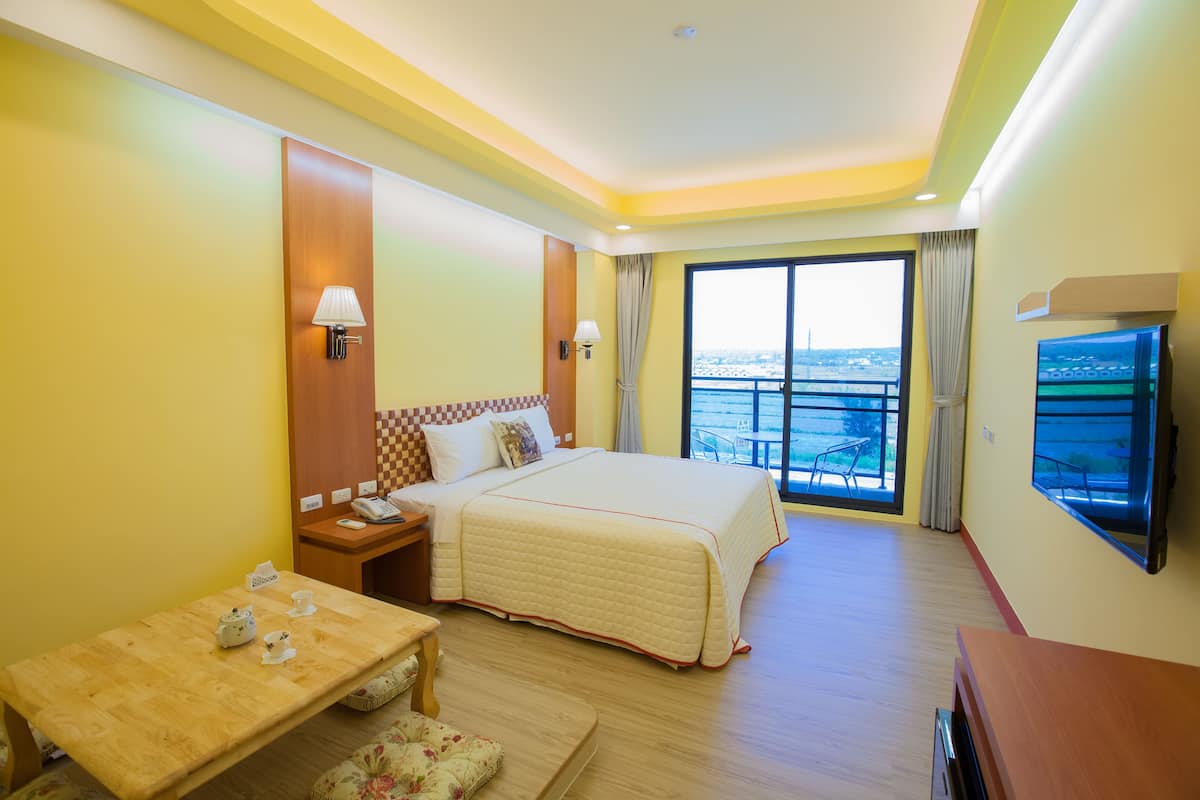 Habitación de hotel con una cama grande, un escritorio, una silla, un televisor y un balcón con vistas.