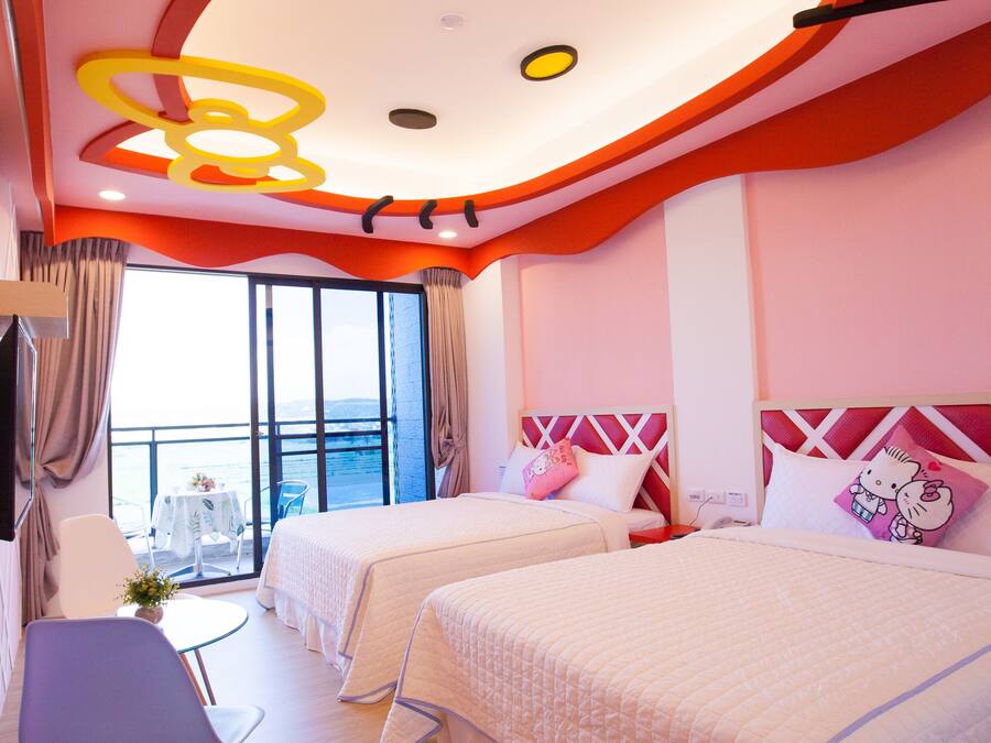 A hotel room with two beds, a chair, a small table with a plant, and a balcony with a table and chairs.