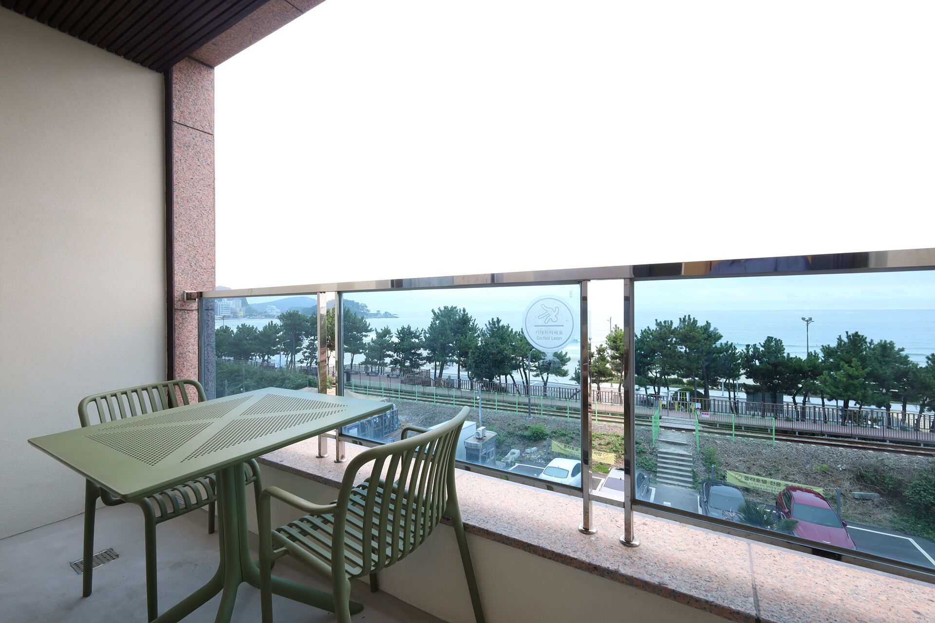 A balcony with a table and chairs, overlooking a coastal area with trees and a view of the sea.
