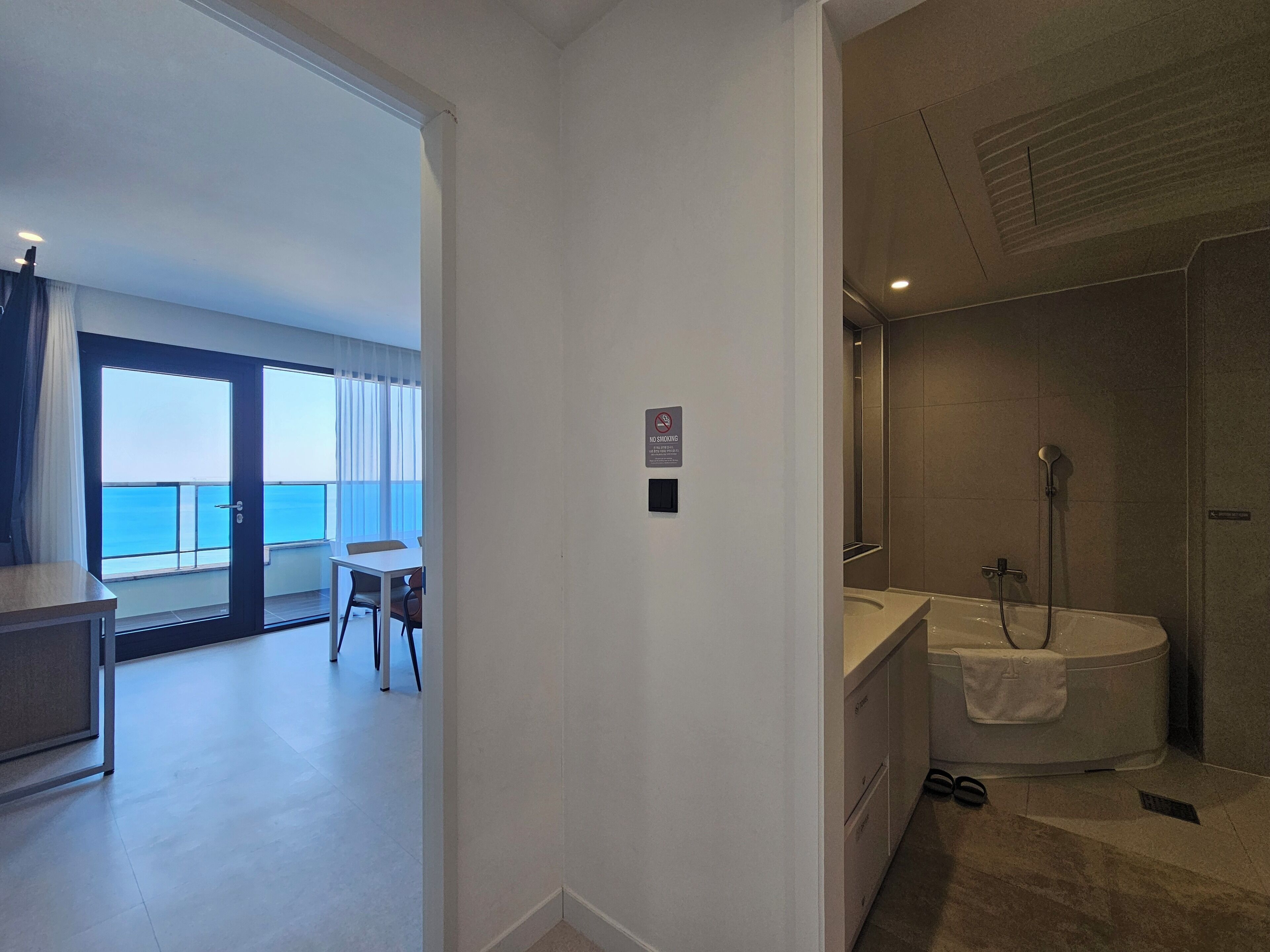 A modern hotel room with a balcony, a shower, and a small dining area.