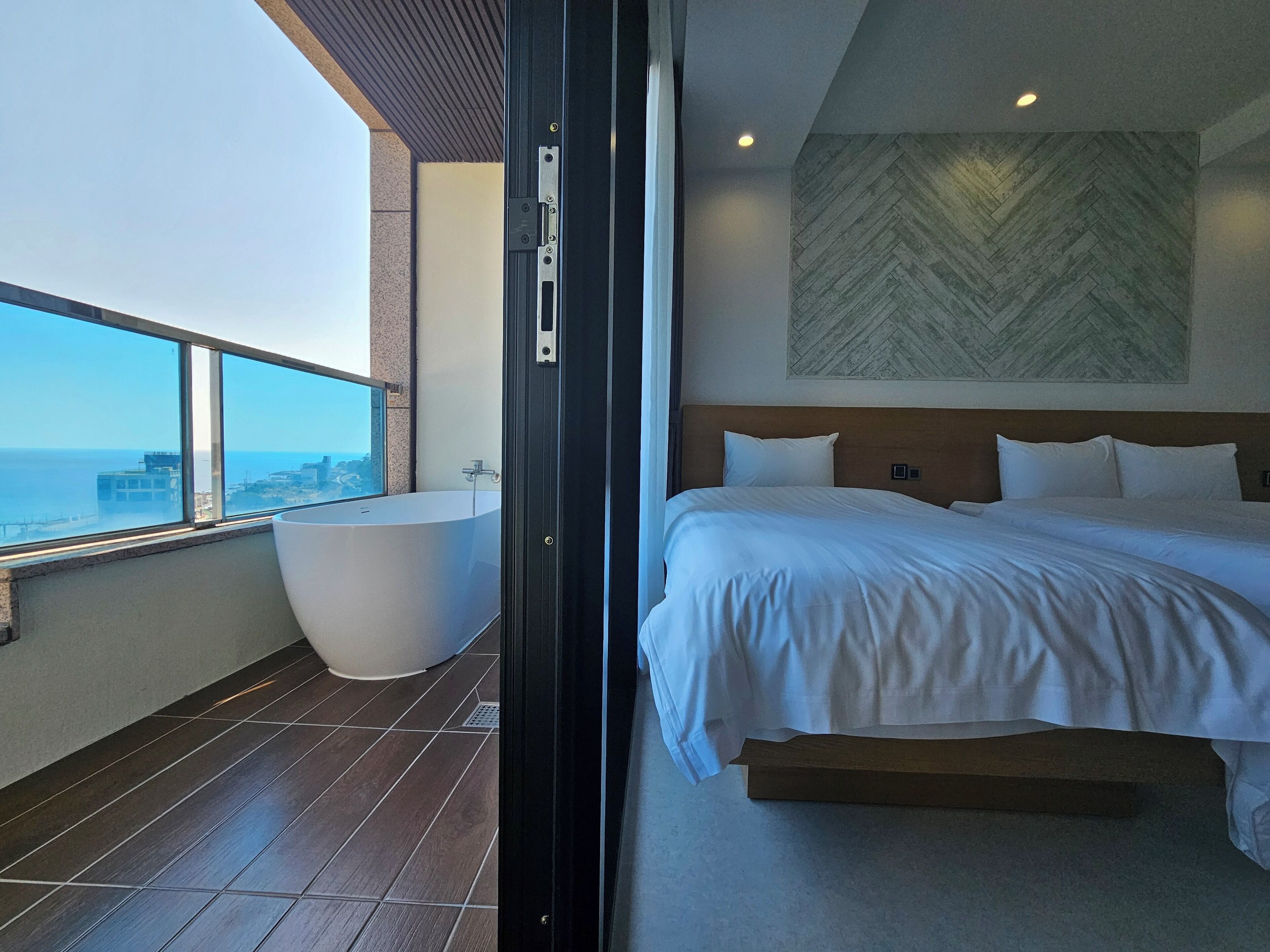 A modern hotel room with a large bed, a view of the city, and a separate bathroom with a bathtub.