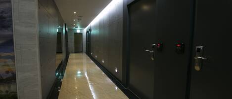 Un pasillo moderno de hotel con piso brillante, paredes oscuras y una puerta grande con cerradura digital.