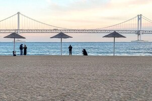 Una playa con sombrillas y gente cerca del agua, un puente al fondo.