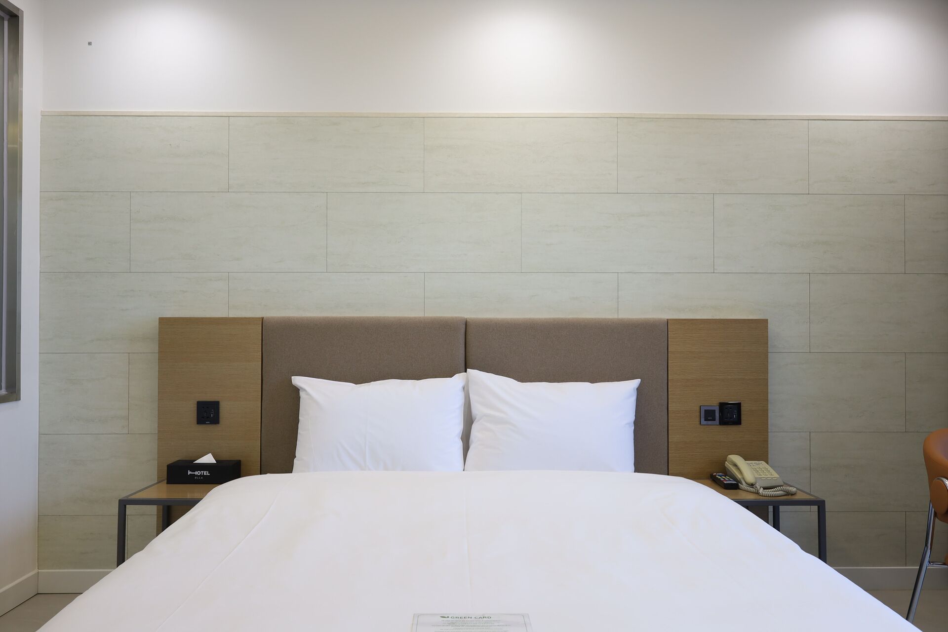 A hotel room with a bed, a nightstand, a telephone, and a wall-mounted control panel.