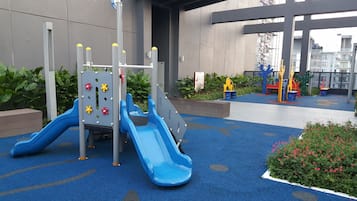 Kids can play on the slide and climbing structure in this outdoor play area with rubber flooring and lush greenery.