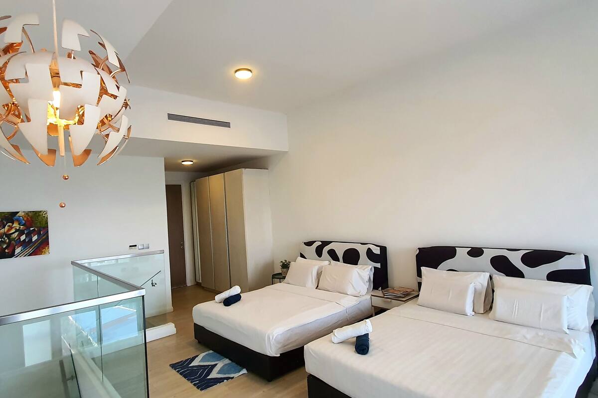 Une chambre d’hôtel moderne avec deux lits, un bureau en verre, un lustre original et un tableau au mur.
