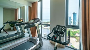 A modern hotel room with a treadmill, exercise bike, and large windows offering a city view. - Greenery Hotel (Da Nang)