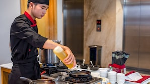 A chef preparing food in a kitchen with a stove, frying pan, and various cooking utensils. - Greenery Hotel (Da Nang)