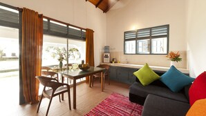 A modern kitchen with a window, a dining area with a table and chairs, and a living area with a sofa and cushions. - Isle Of Thalpe (Unawatuna)