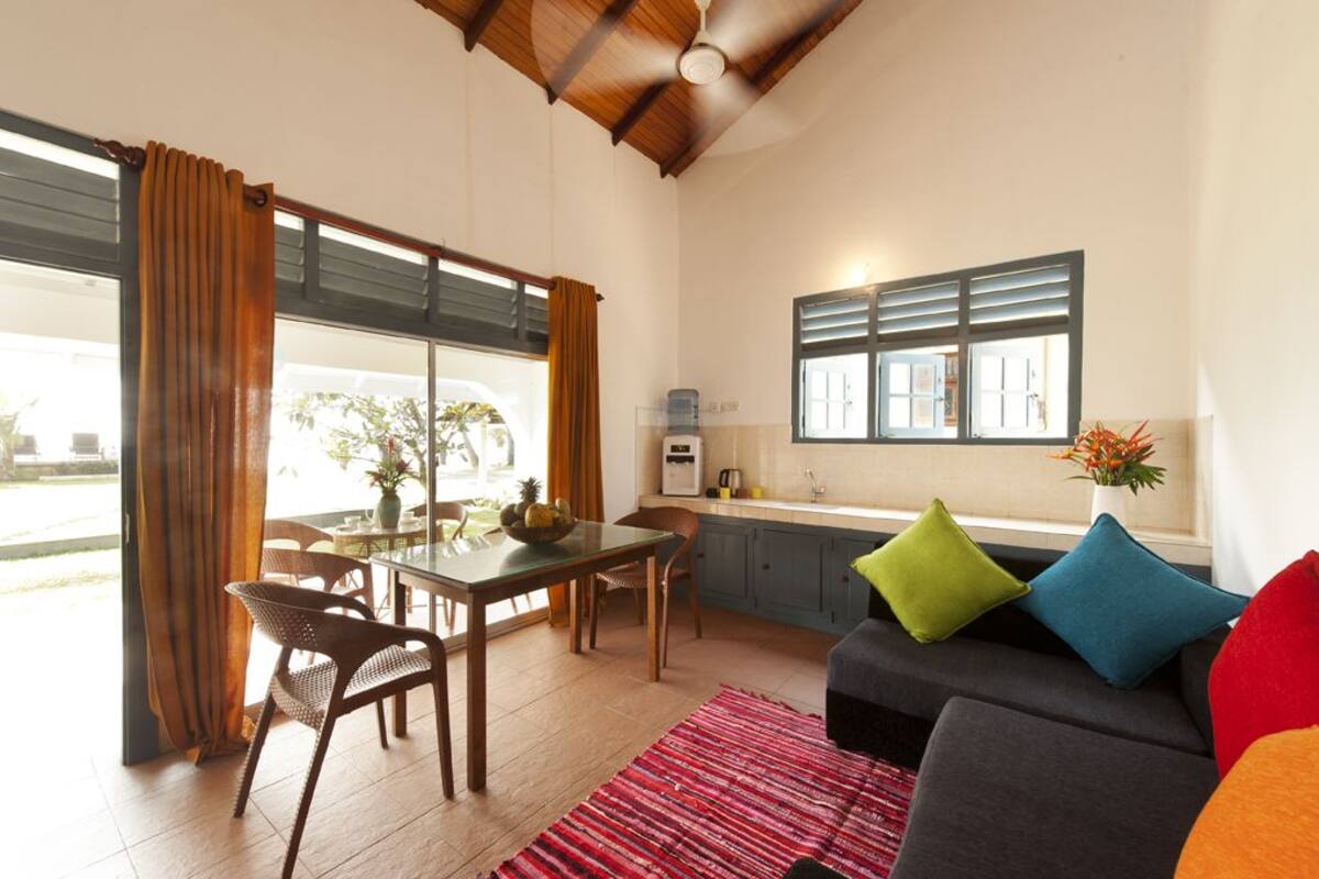 Eine moderne Küche mit Fenster, ein Essbereich mit Tisch und Stühlen sowie eine Wohnbereits mit Sofa und Kissen.