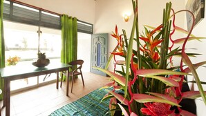 A room with a dining table, chairs, a potted plant, a window with curtains, and a door with a decorative panel. - Isle Of Thalpe (Unawatuna)
