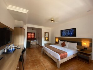 A hotel room with a bed, bedside tables, a TV, and a desk with a chair. - Chalston Beach Resort (Calangute)