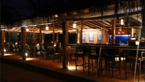 An outdoor dining area with tables and chairs, a bar area with a counter, and a thatched roof structure. - Chalston Beach Resort (Calangute)