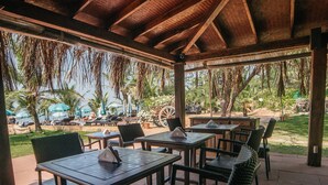 An outdoor patio with tables and chairs, surrounded by palm trees and a view of the ocean. - Chalston Beach Resort (Calangute)