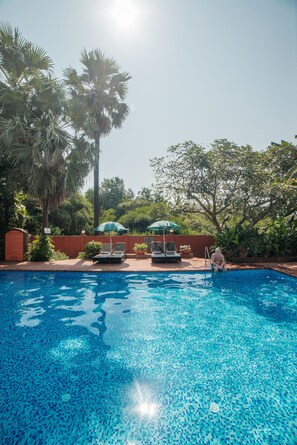 A swimming pool with lounge chairs and umbrellas, surrounded by palm trees and greenery. - Chalston Beach Resort (Calangute)