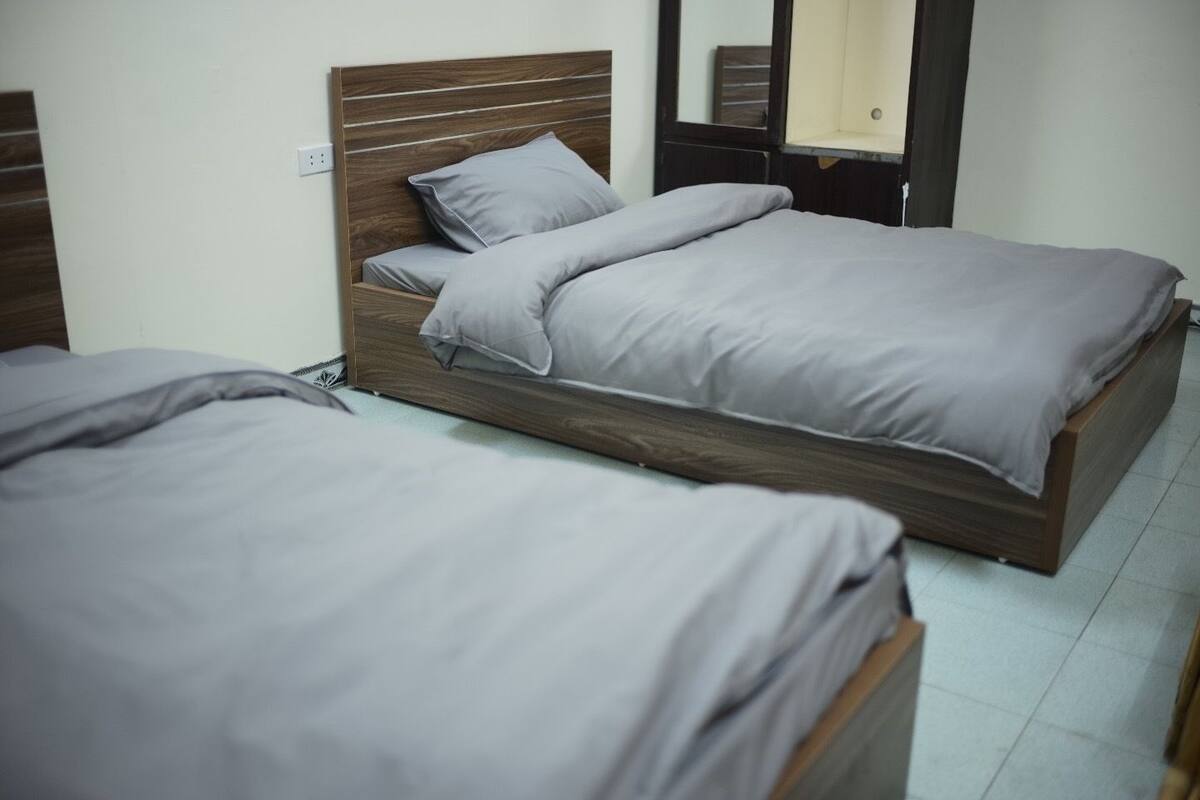 Una habitació amb dos llits individuals, cadascun amb un capçal de fusta i roba de llit gris.