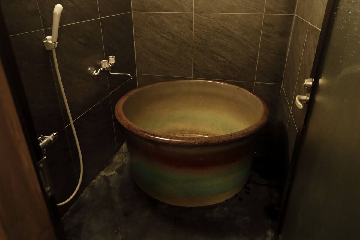 Une salle de bain avec des toilettes en céramique, une pomme de douche et un mur carrelé.
