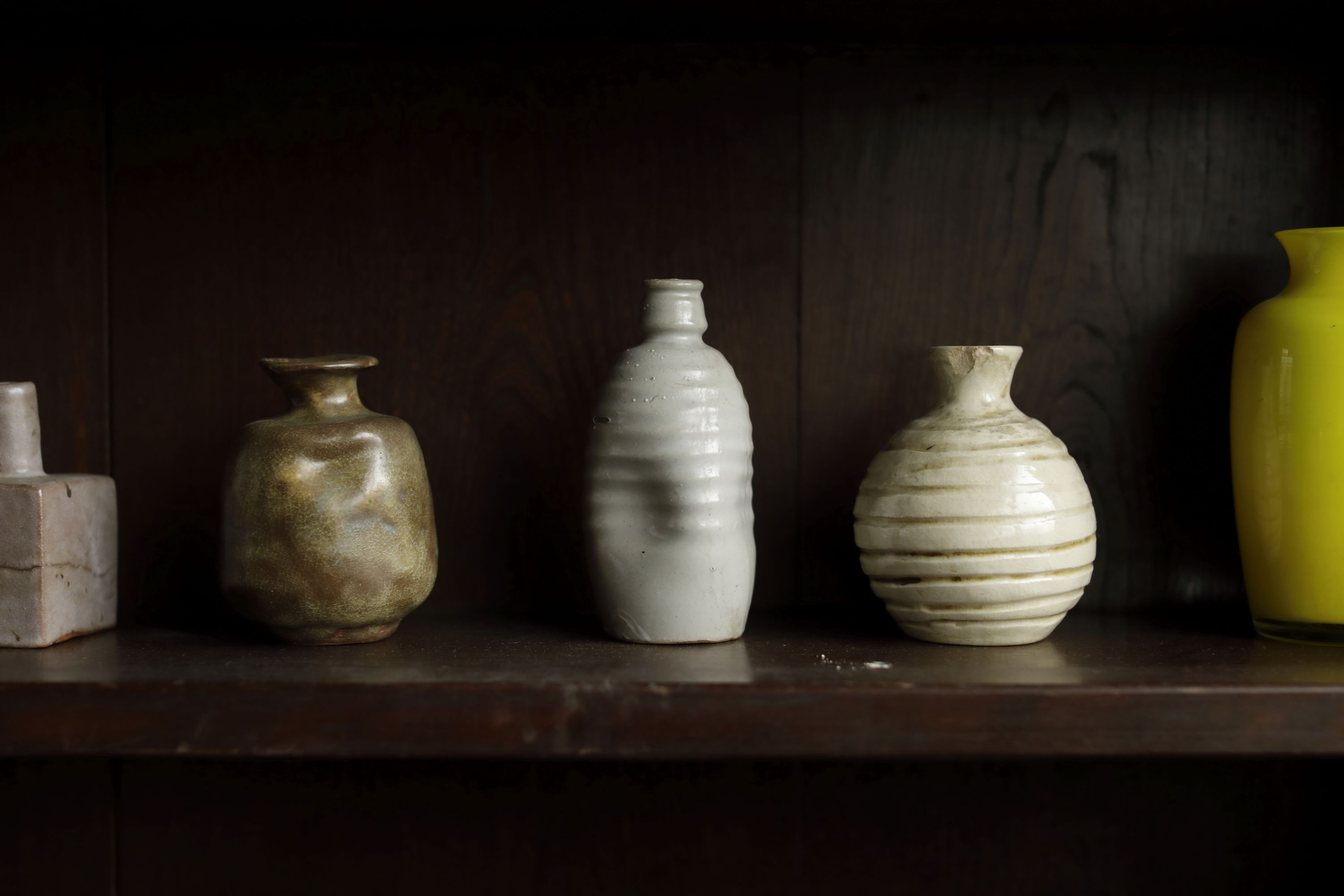 Four ceramic vases of varying shapes and sizes on a wooden shelf.