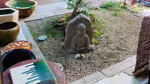 Un jardin de style japonais traditionnel, agrémenté d’un petit arbre, d’une statue de pierre et de diverses plantes en pot.