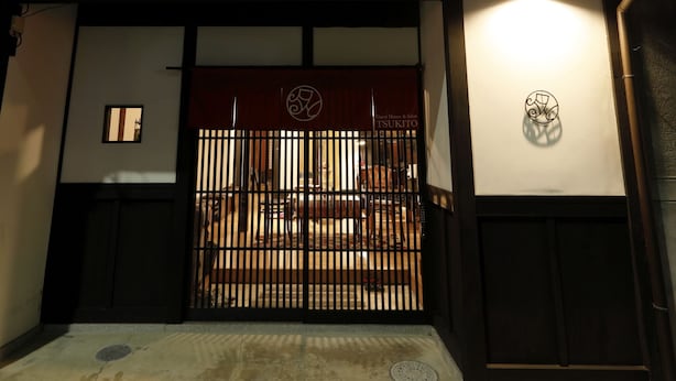 Un bâtiment traditionnel japonais doté d’une porte en bois, d’un balcon et d’une enseigne avec un logo.