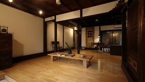 Une pièce de style japonais traditionnel, avec un plancher en bois, une petite table sur laquelle sont posés des livres et un vase, et une porte coulissante qui donne sur une autre pièce.