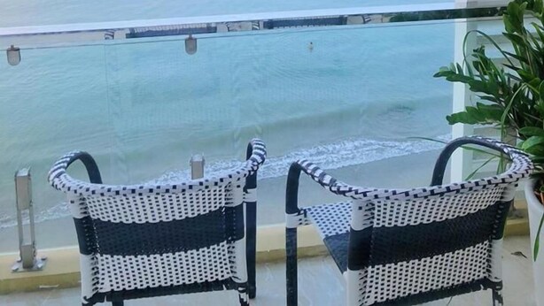 A balcony with two wicker chairs and a small table, overlooking a calm sea and distant mountains. - Vivu Hotel (Quy Nhon)