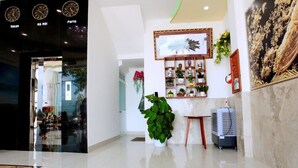 A lobby with a large mirror, a potted plant, a framed artwork, and a wall-mounted clock. - Vivu Hotel (Quy Nhon)