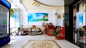 A hotel lobby with a large, ornate carpet, a sofa, a wooden cabinet, and a Pepsi refrigerator. - Vivu Hotel (Quy Nhon)