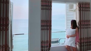 A room with a large window, curtains, an air conditioning unit, and a view of the sea. - Vivu Hotel (Quy Nhon)