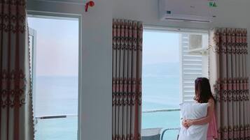 A room with a large window, curtains, an air conditioning unit, and a view of the sea.
