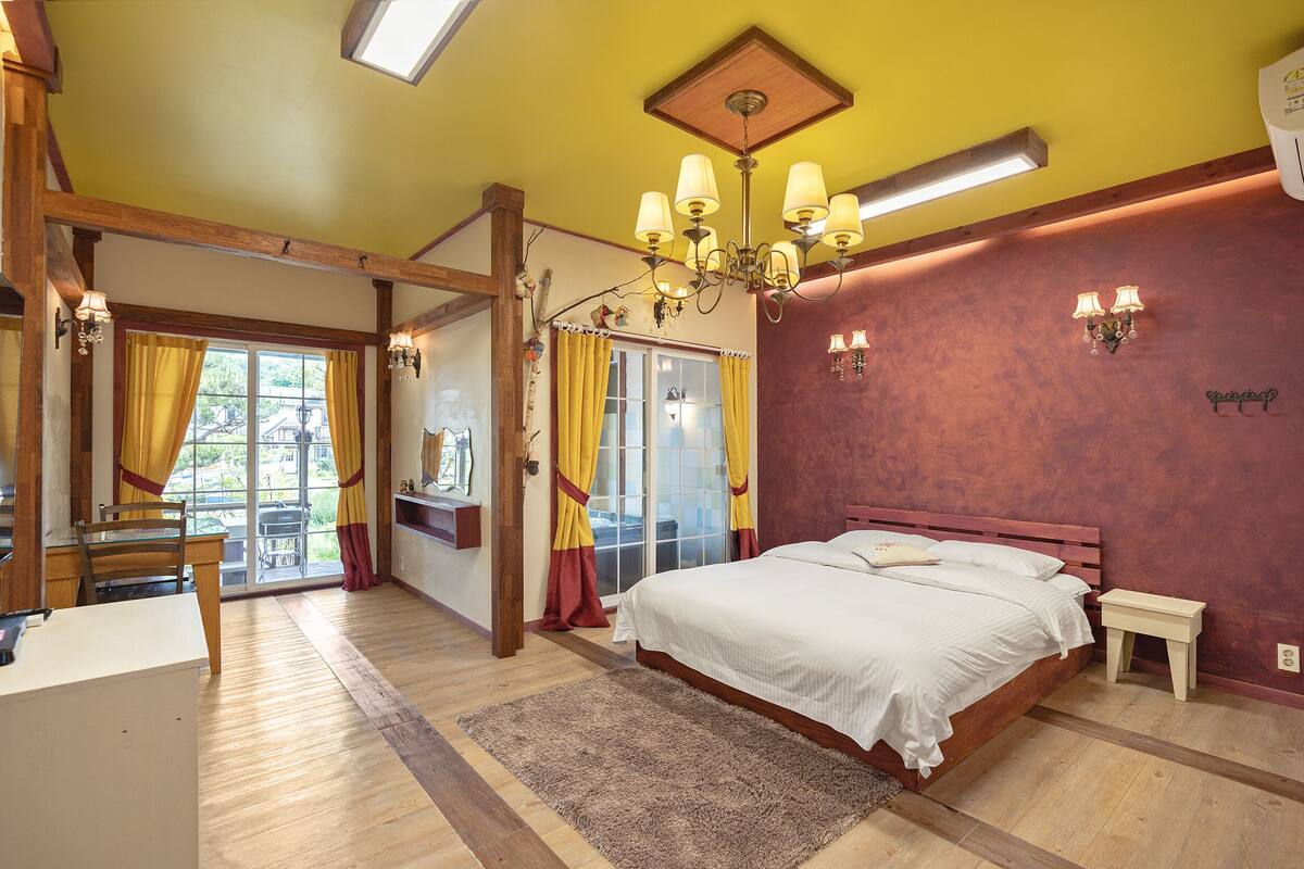 A bedroom with a large bed, wooden beams, a chandelier, and a view through a glass door.