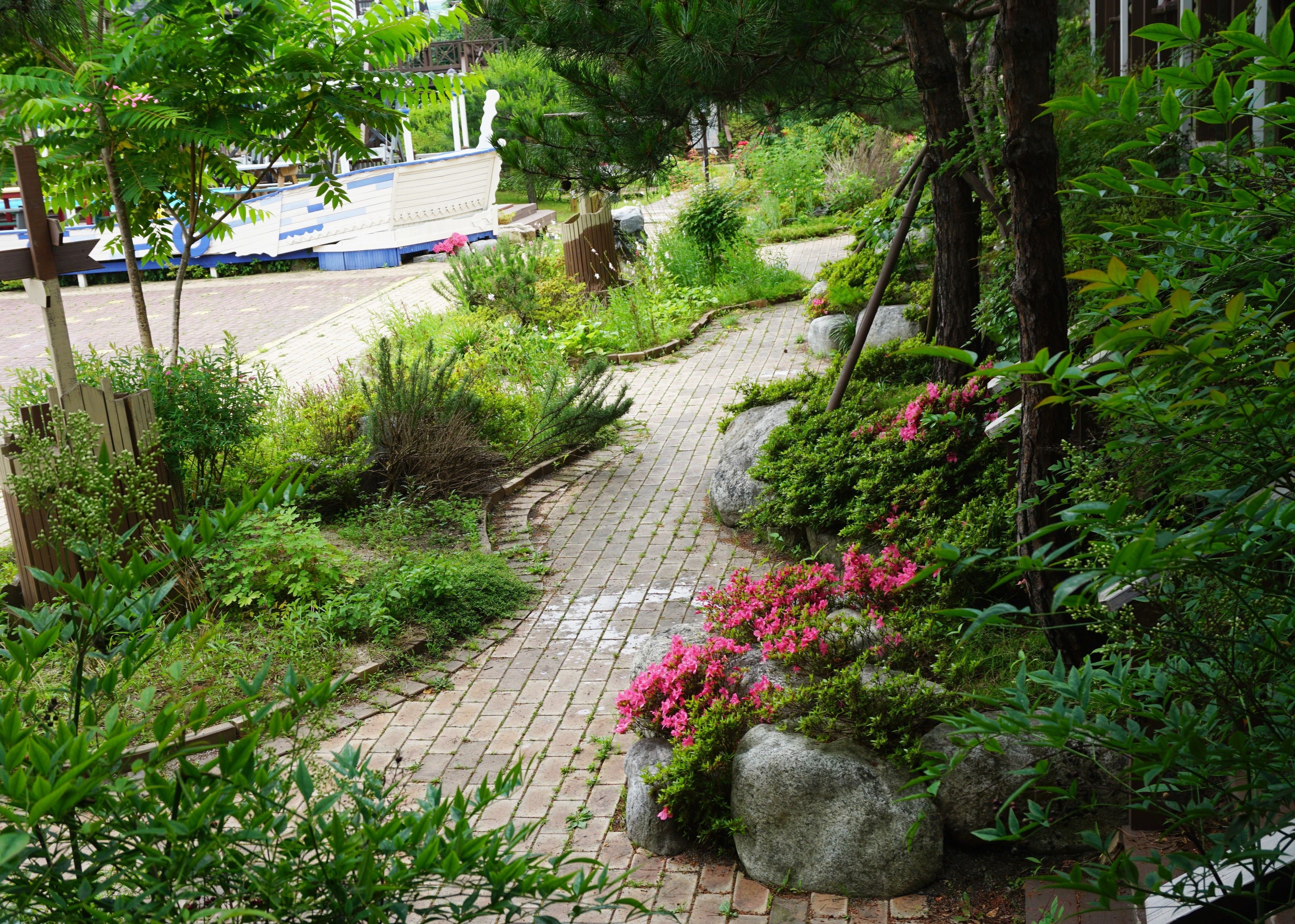 Ein Gartenweg mit einer Bank, umgeben von üppigem Grün und blühenden Pflanzen.