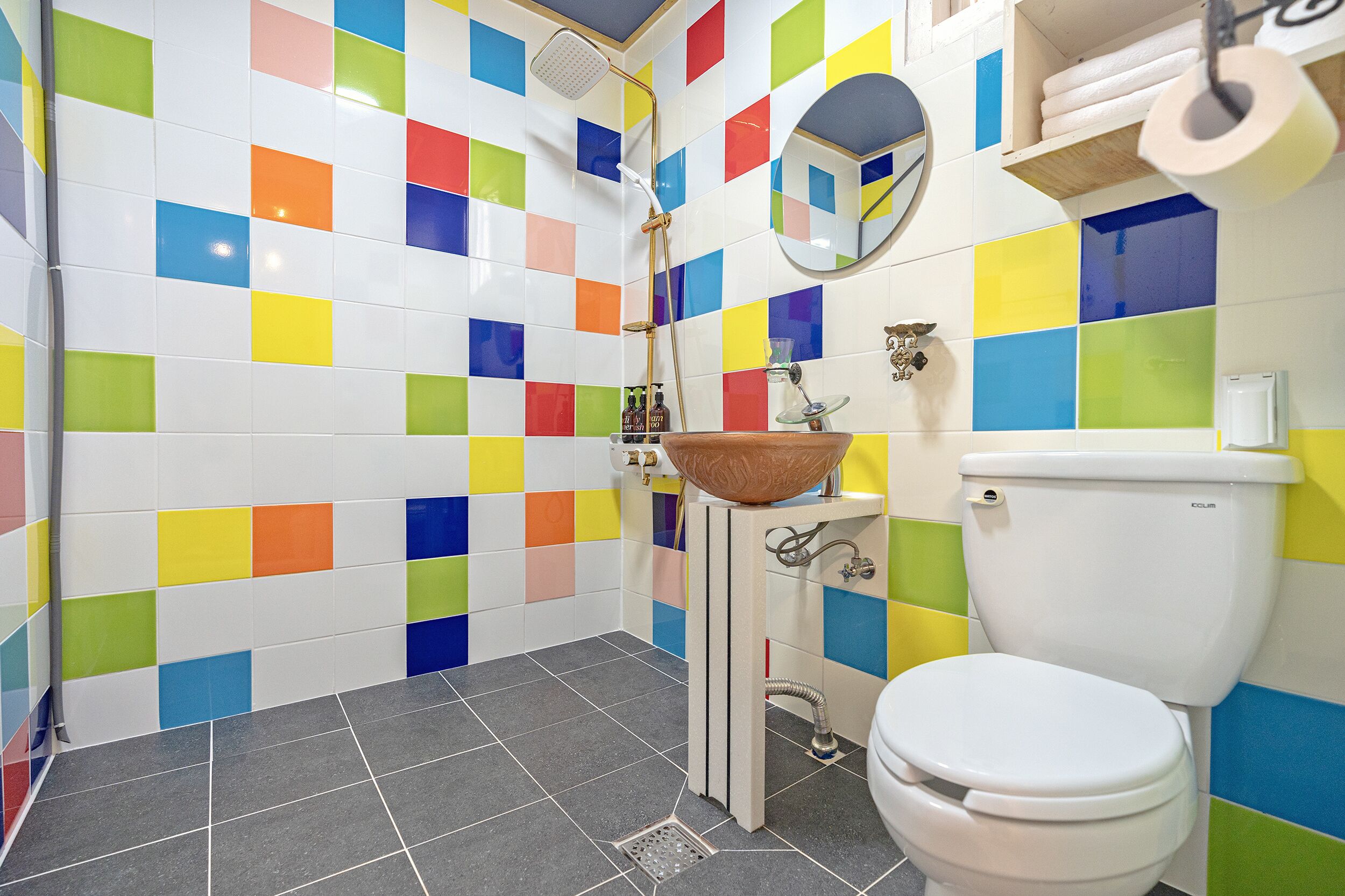 Een badkamer met kleurrijke tegels, een wastafel met kom, een toilet en een douche.