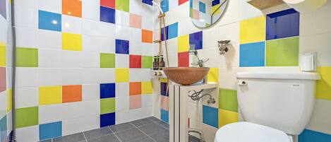 Een badkamer met kleurrijke tegels, een wastafel met kom, een toilet en een douche.