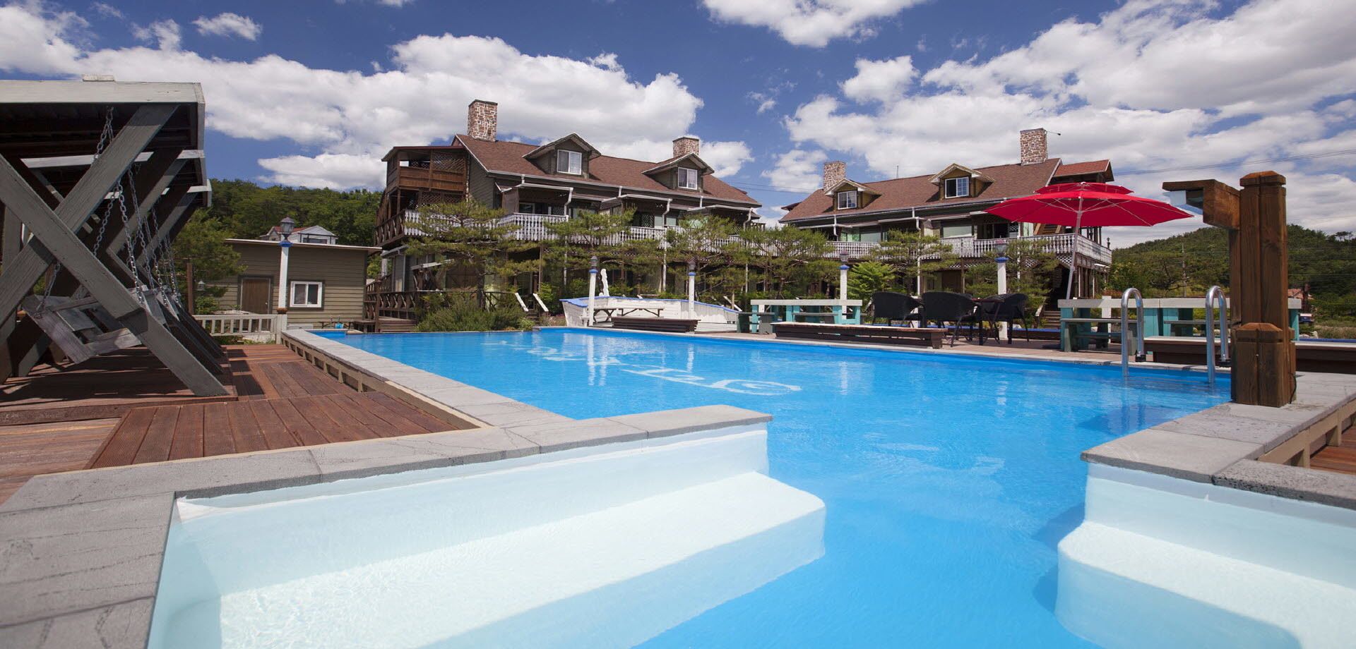 A swimming pool with a wooden deck and a view of a resort building with multiple chimneys and balconies.