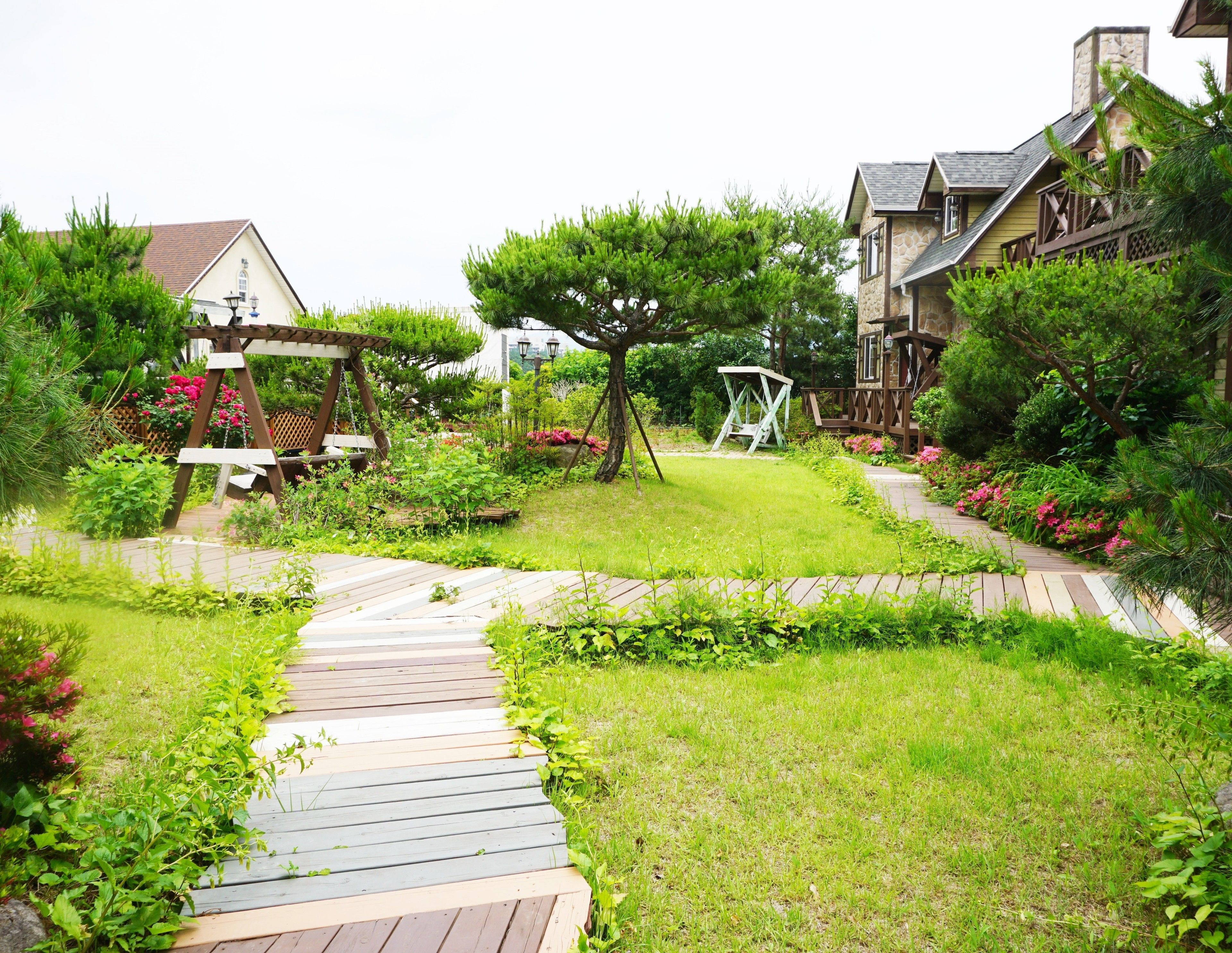 A garden pathway leading to a wooden gazebo, surrounded by lush greenery and flowering plants.