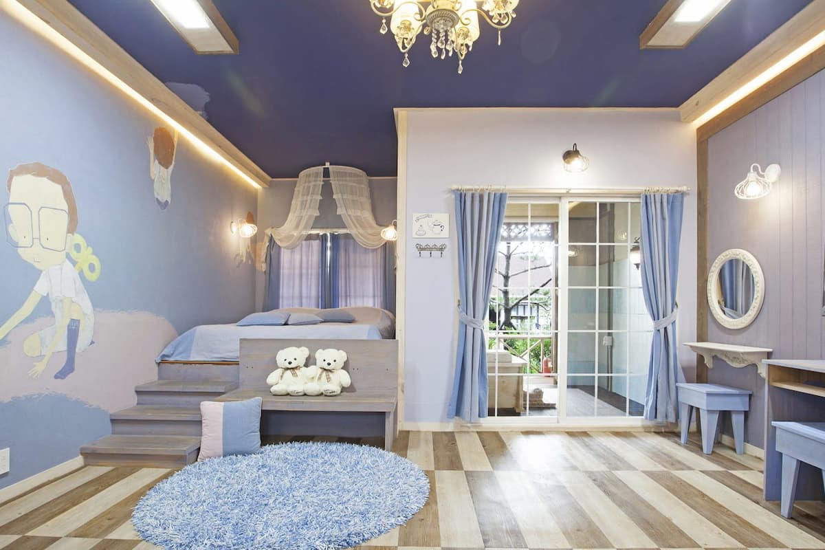A child's bedroom with a bed, a teddy bear, a chandelier, and a large window.