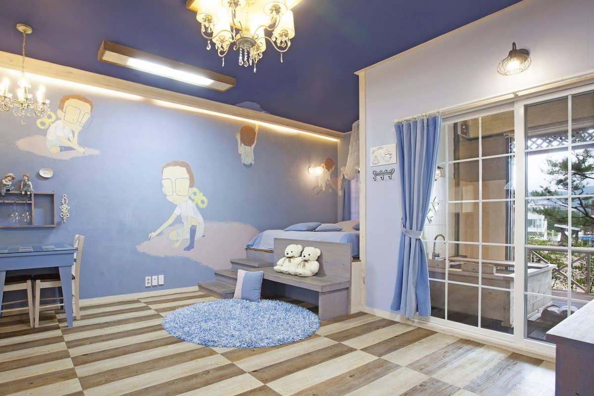 A room with a checkered wooden floor, a blue sofa, a desk with a chair, a chandelier, and a large window with curtains.