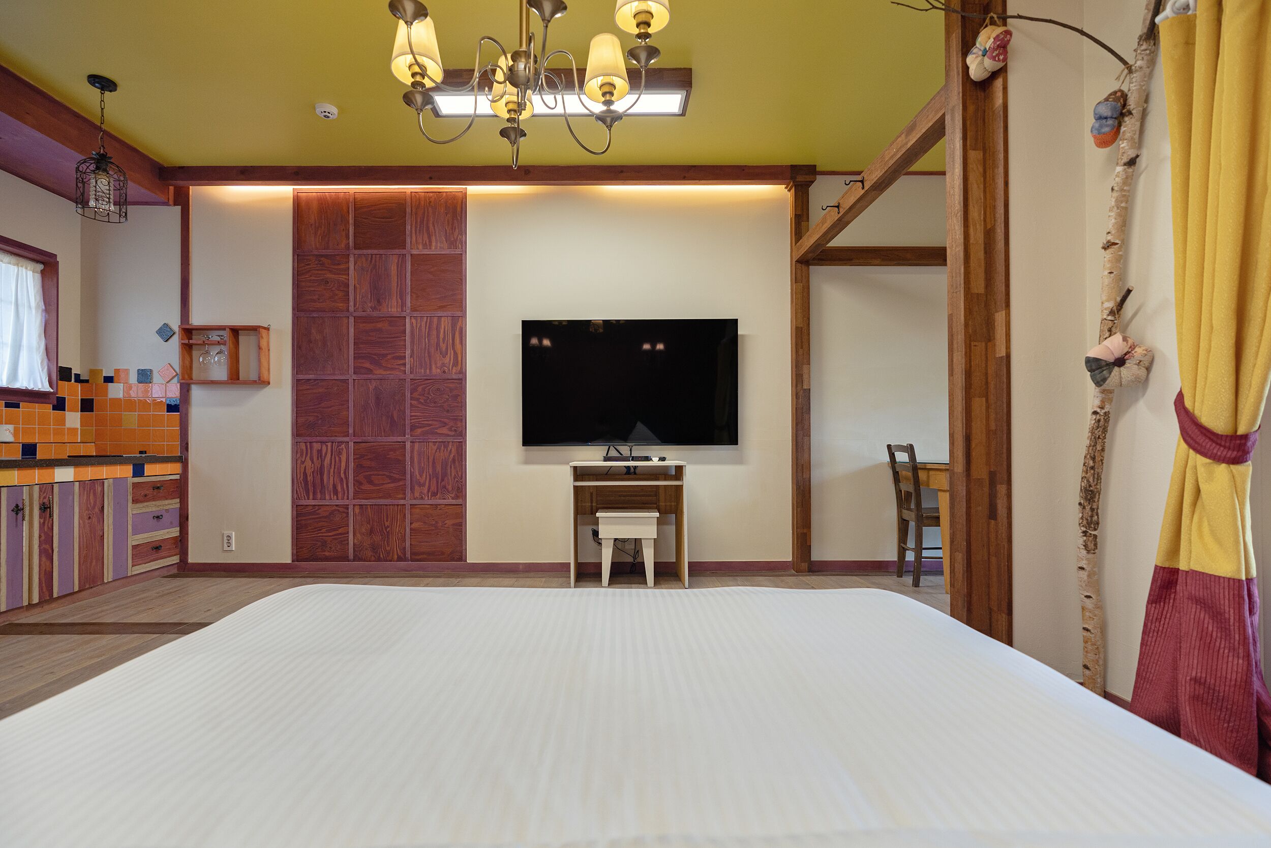 Un dormitorio con una cama grande, un televisor montado en la pared, un escritorio de madera y una silla.