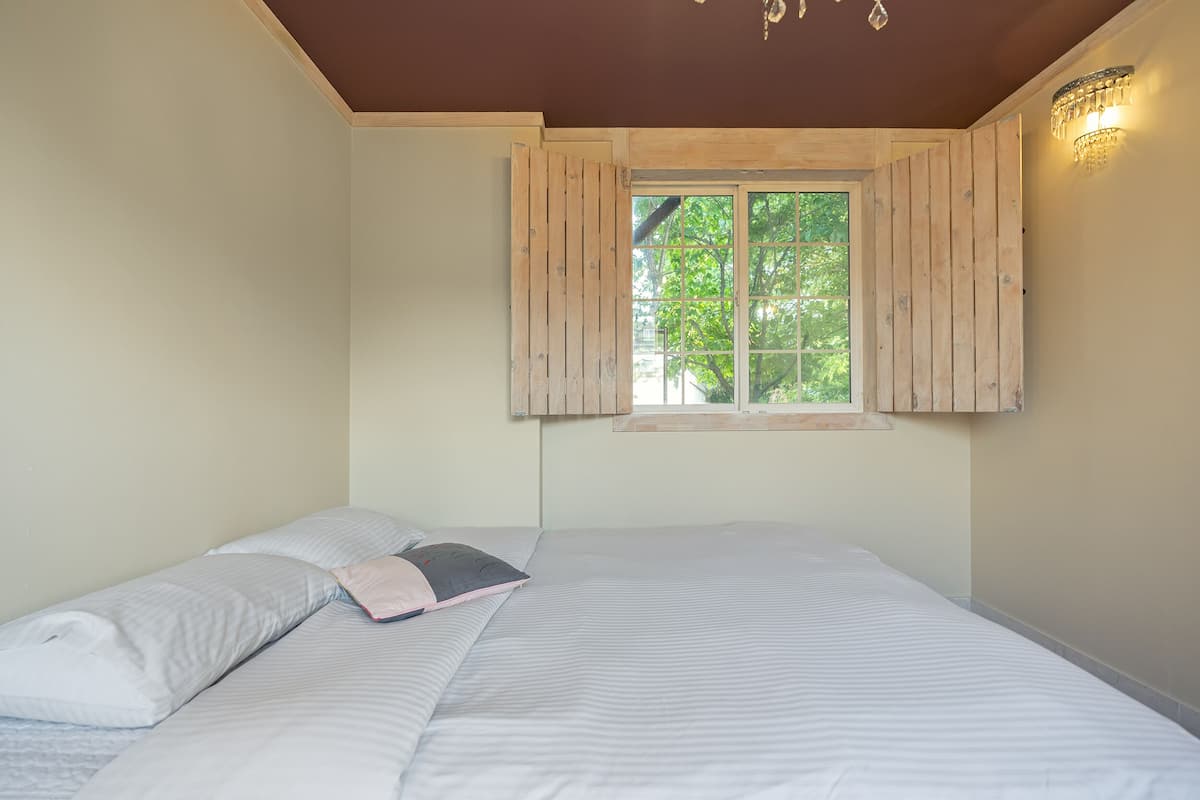A bedroom with a large bed, wooden shutters on the window, and a chandelier.