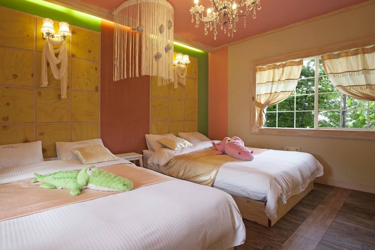 A hotel room with two beds, a chandelier, and a window with curtains.