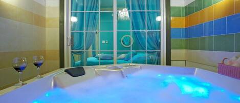 Une pièce dotée d’un grand jacuzzi éclairé, d’une fenêtre avec des rideaux et d’un mur orné d’un motif coloré en carreaux.