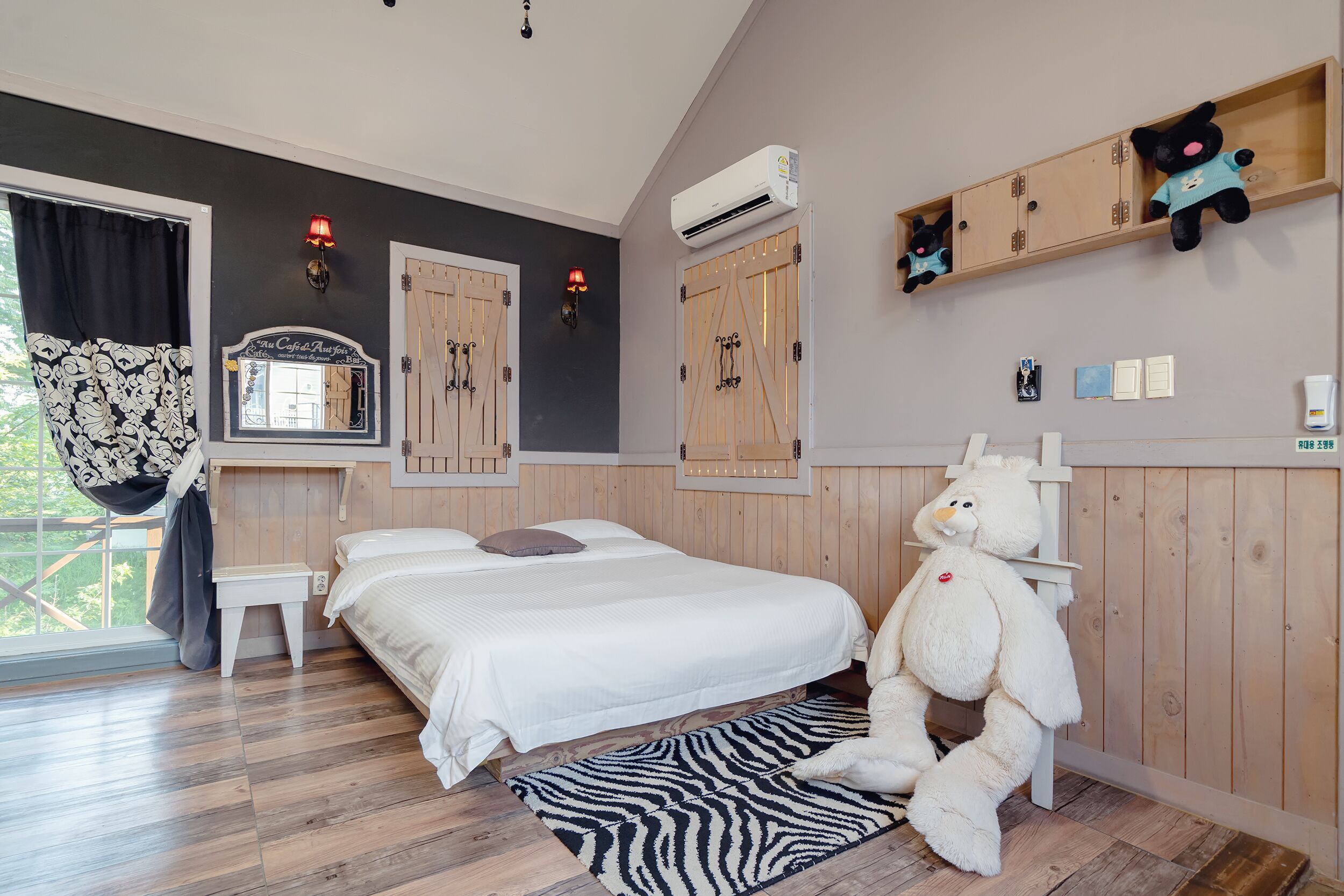 A bedroom with a large bed, a zebra-patterned rug, wooden walls, and a teddy bear on the floor.