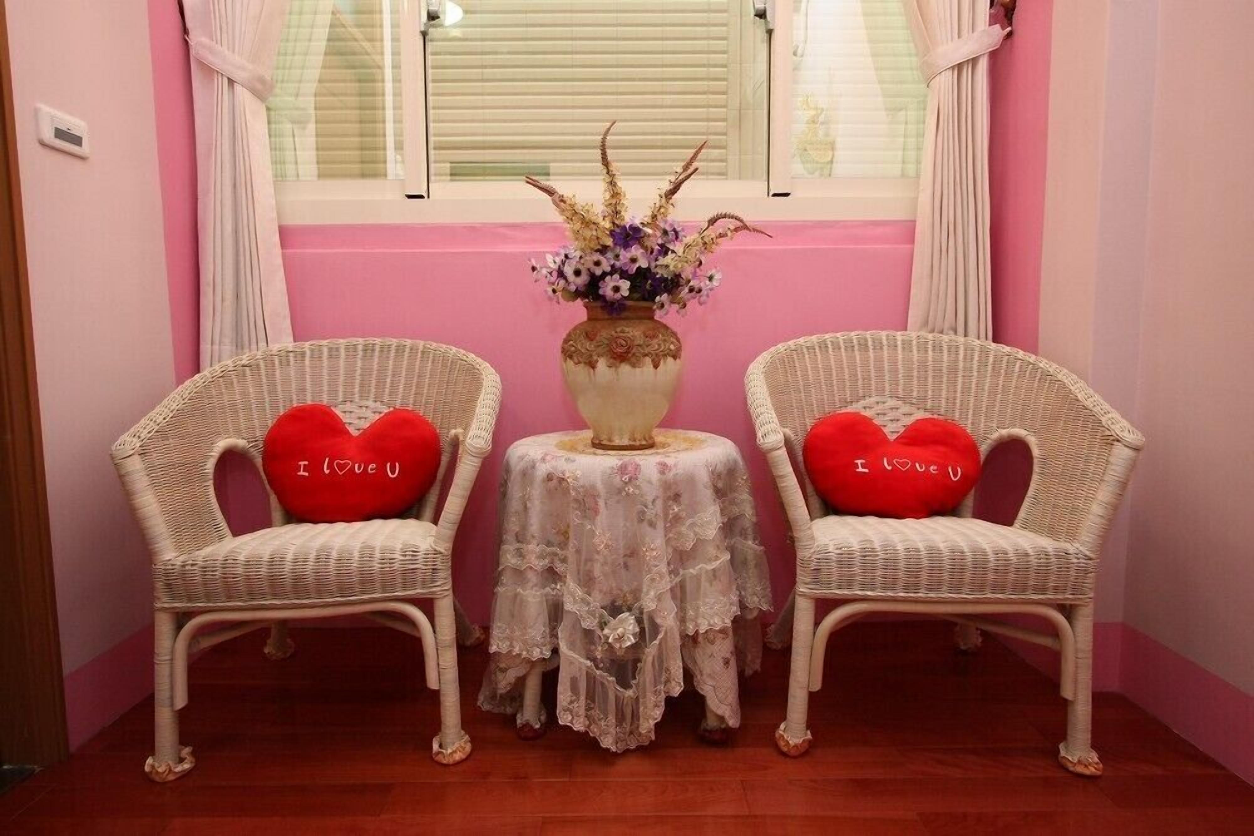 Two wicker chairs with heart-shaped cushions and a small table with a floral centerpiece between them.