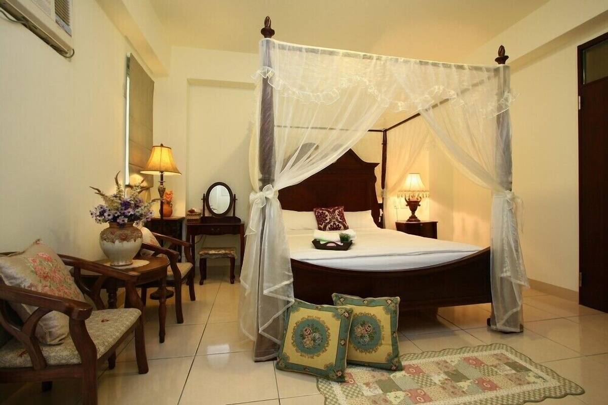 A four-poster bed with a canopy, a wooden nightstand, a bedside table with a lamp, and a floral vase.