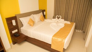 A neatly made bed with a heart-shaped towel arrangement, a bedside phone, and a lamp on a wooden nightstand.