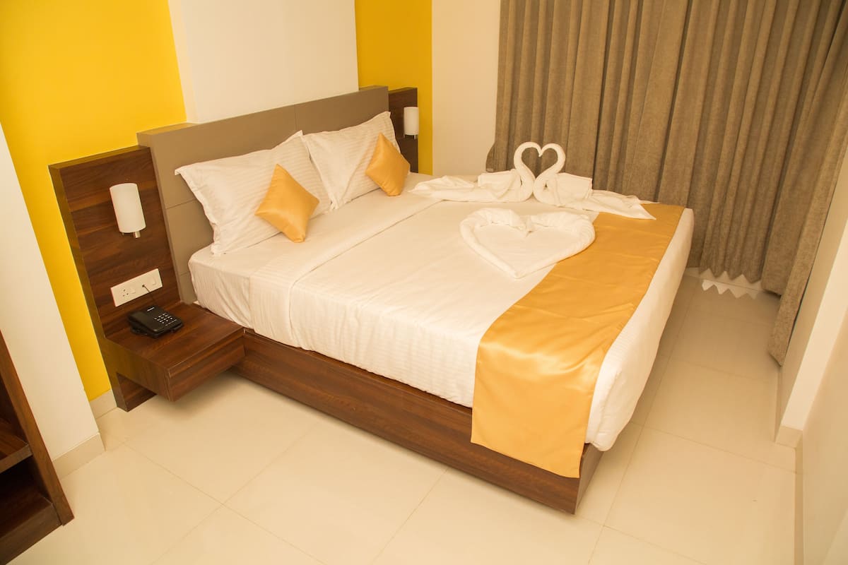 A neatly made bed with a heart-shaped towel arrangement, a bedside phone, and a lamp on a wooden nightstand.