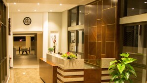A hotel lobby with a reception desk, a seating area with a sofa and a coffee table, and a large plant.
