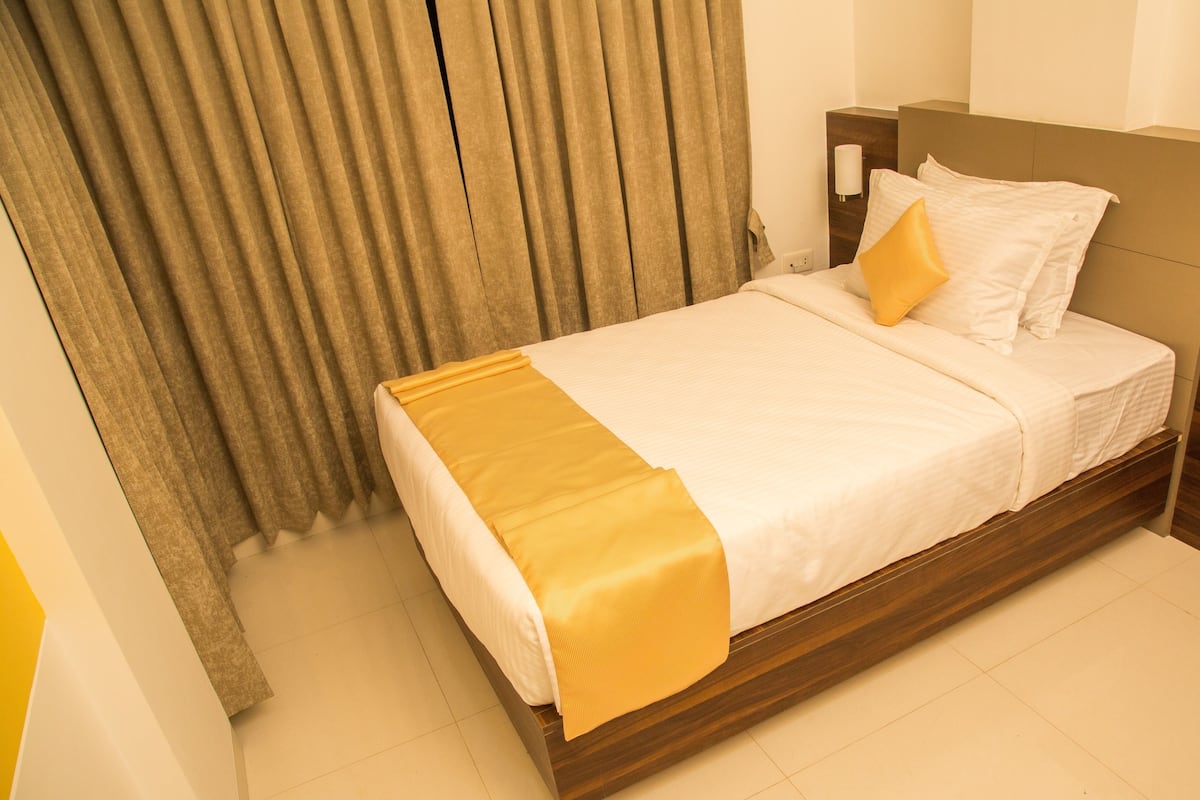 A neatly made bed with a yellow throw blanket, a wooden headboard, and a bedside lamp.