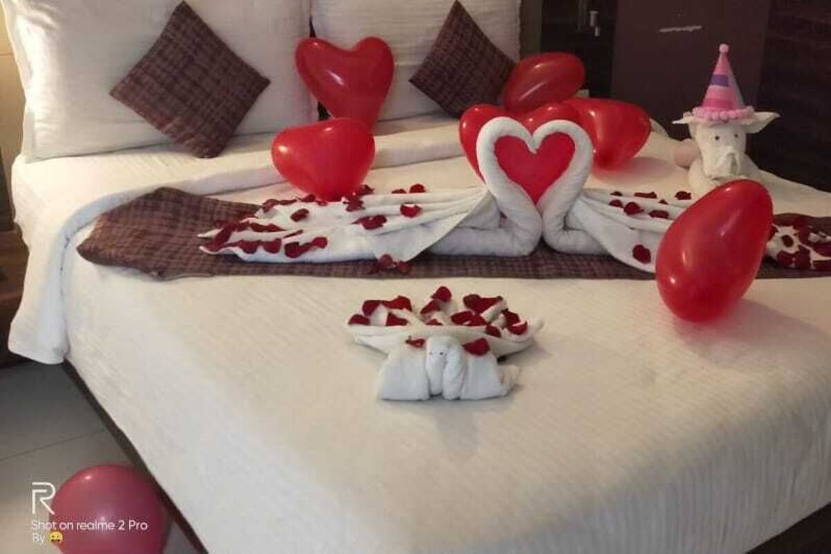 A neatly made bed with heart-shaped decorations, a small white figurine, and a pink party hat.